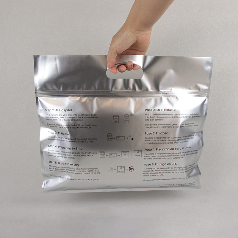 Hand holding large silver metallic resealable zipper bag with printed bilingual English and Spanish instruction text, carry handle on top, medical return packaging pouch